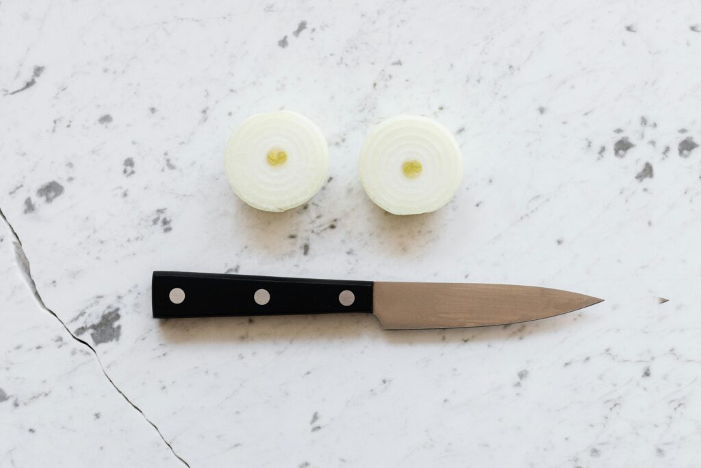 sharp chef knife on a cutting board next to a halved onion